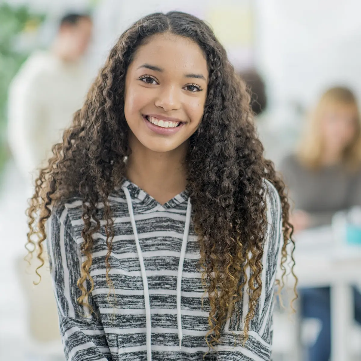 A young woman with curly hair smiles brightly.
