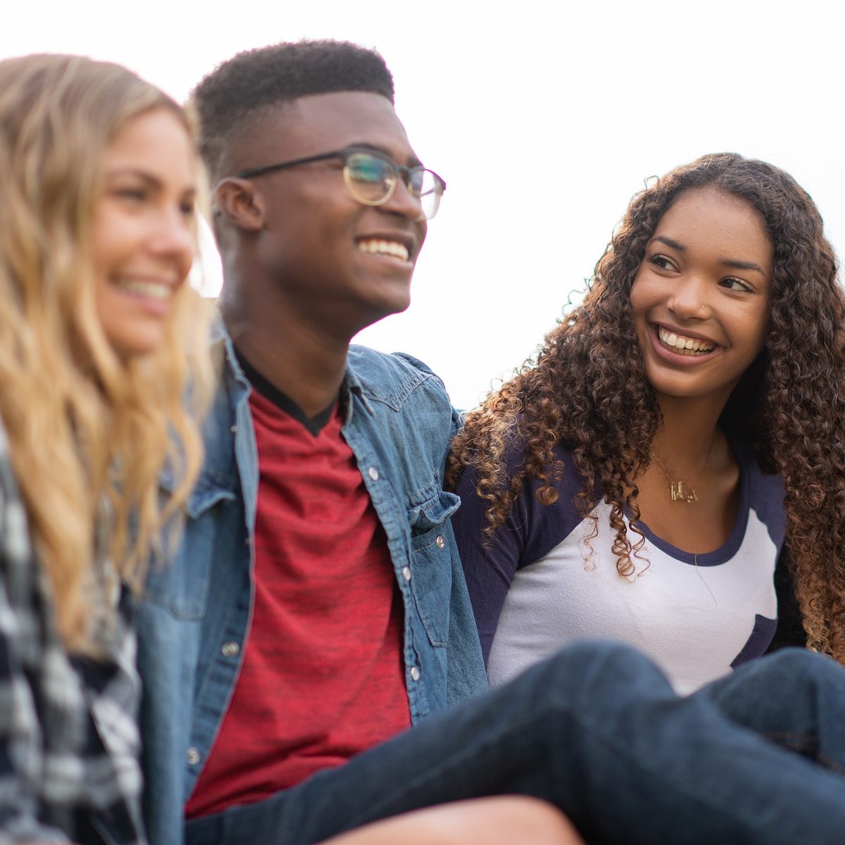 A group of four young people sitting closely on a bench, sharing laughter and conversation in a vibrant outdoor environment.