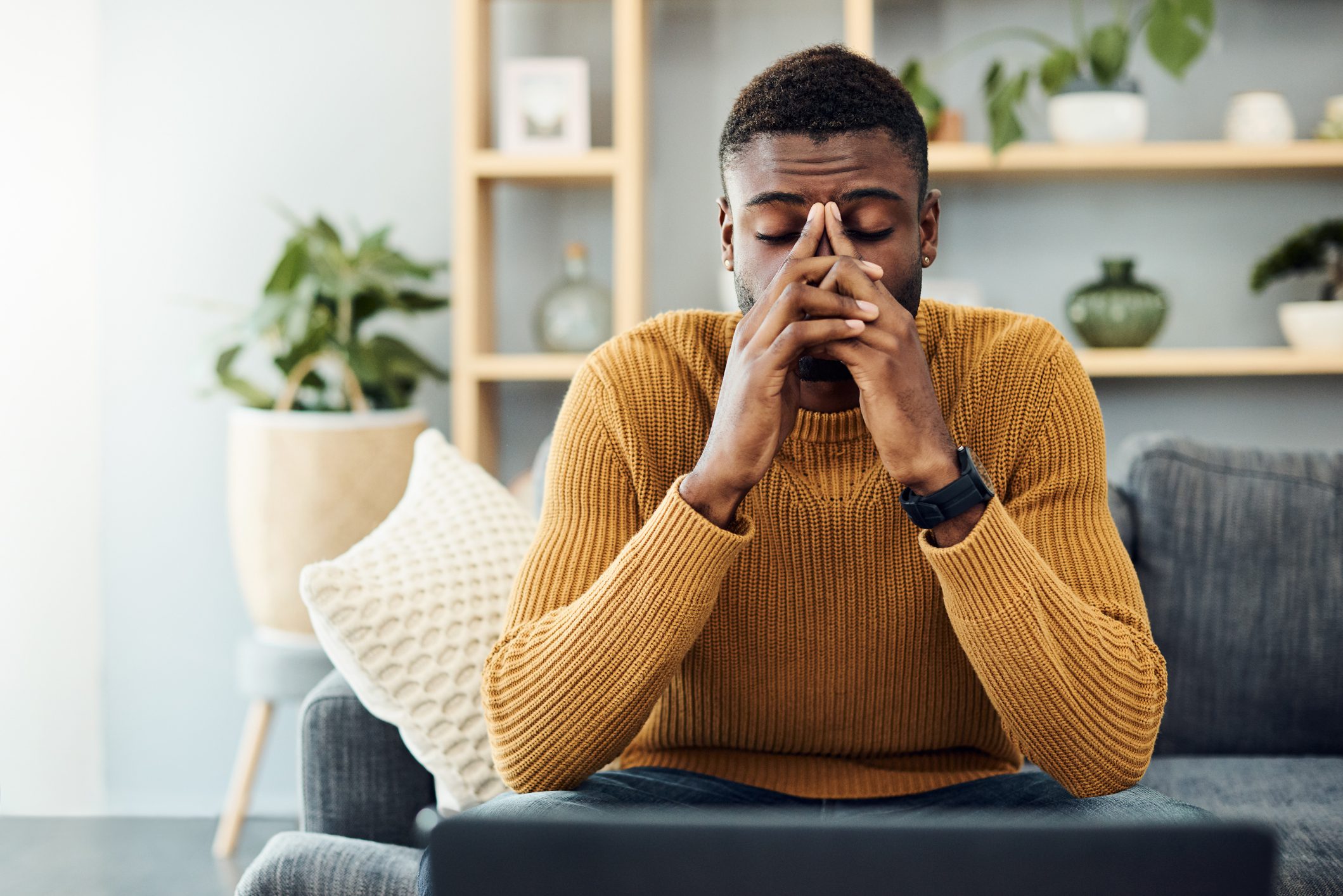 Stressed African American man sits on sofa with his head in his hands