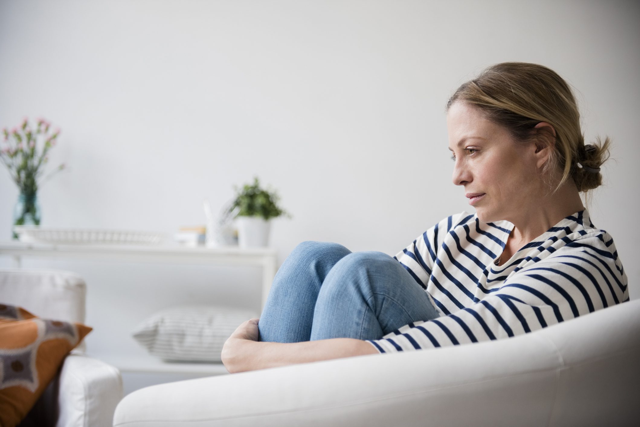 A depressed woman hugs her legs while sitting in her living room.